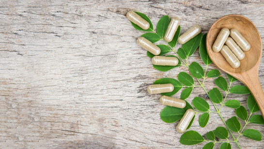 supplements in wooden spoon on top of plant supplied by Natural Medicine Doctor in Downers Grove IL